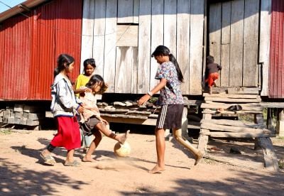 A young girl fitted with a prothesis is playing football with her sibblings in front of her small house