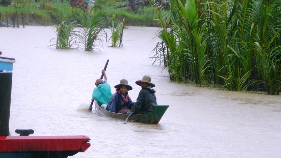 Trois personnes sont assises dans un petit bateau sur une rivière débordante. 