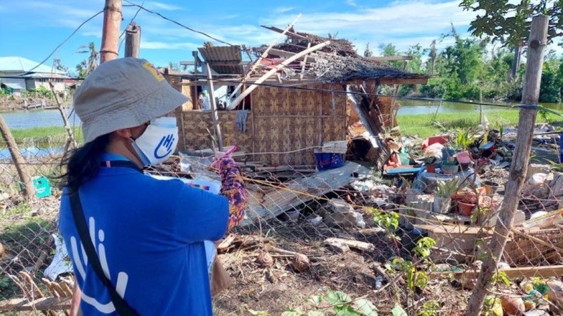 Une femme portant un masque se tient devant une maison en ruine 