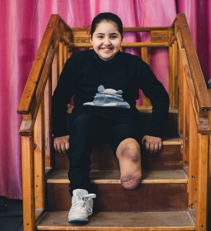 A young disabled girl sits and smiles. 