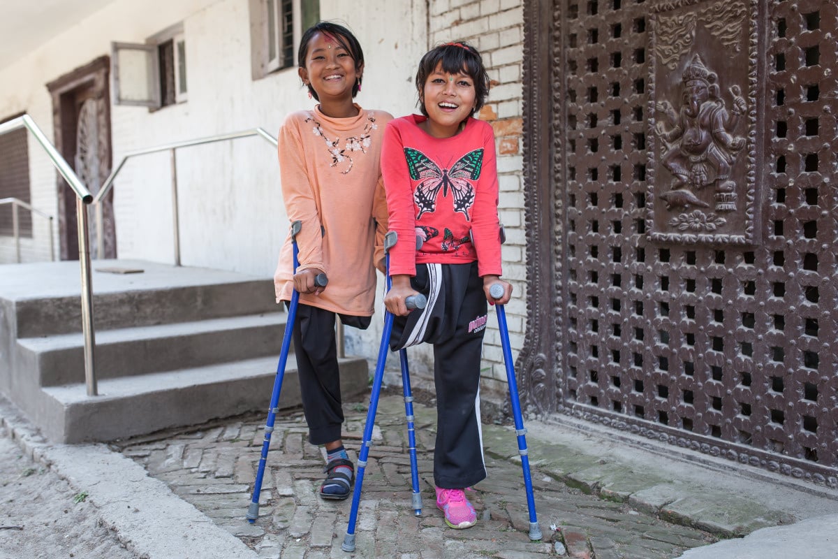 Deux filles souriantes, appuyées sur des béquilles.