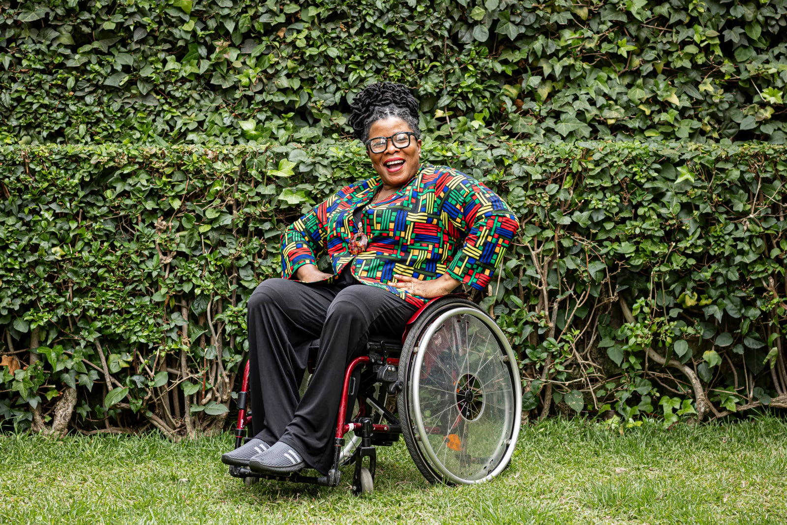 A woman in a wheelchair, outside, facing the camera, smiling