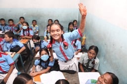 Une fille souriante qui lève la main dans une salle de classe.