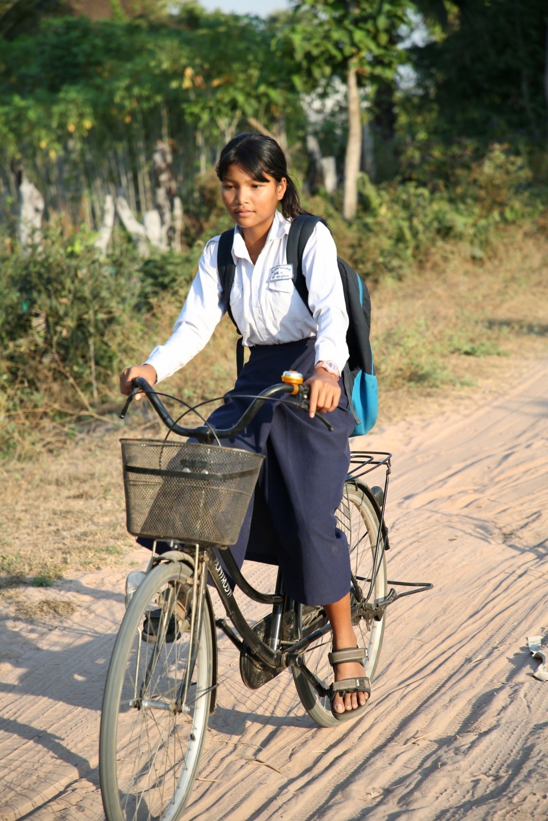 Une jeune fille appareillée avec une prothèse fait du vélo sur une route en terre