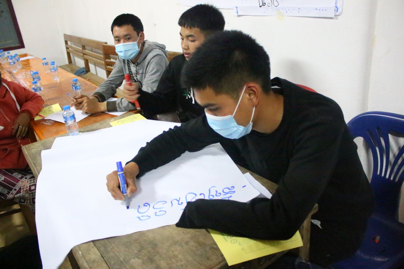 Joc at school writing on a poster, with his classmates.