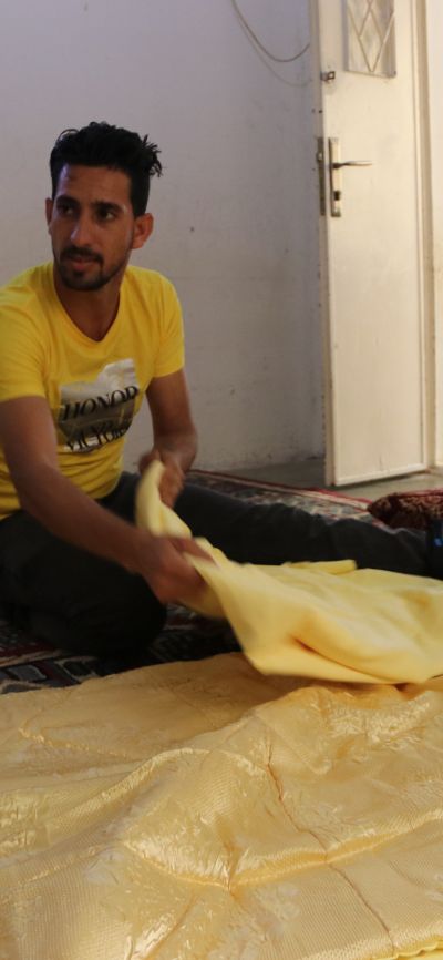 Ahmad montre la literie qu'il a fabriquée dans son entreprise à domicile. © D.Ginsberg / HI