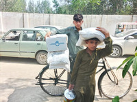 Un garçon tient un kit alimentaire HI à l'arrière d'un vélo. Un garçon plus jeune porte des provisions alimentaires dans sa main et sur sa tête.