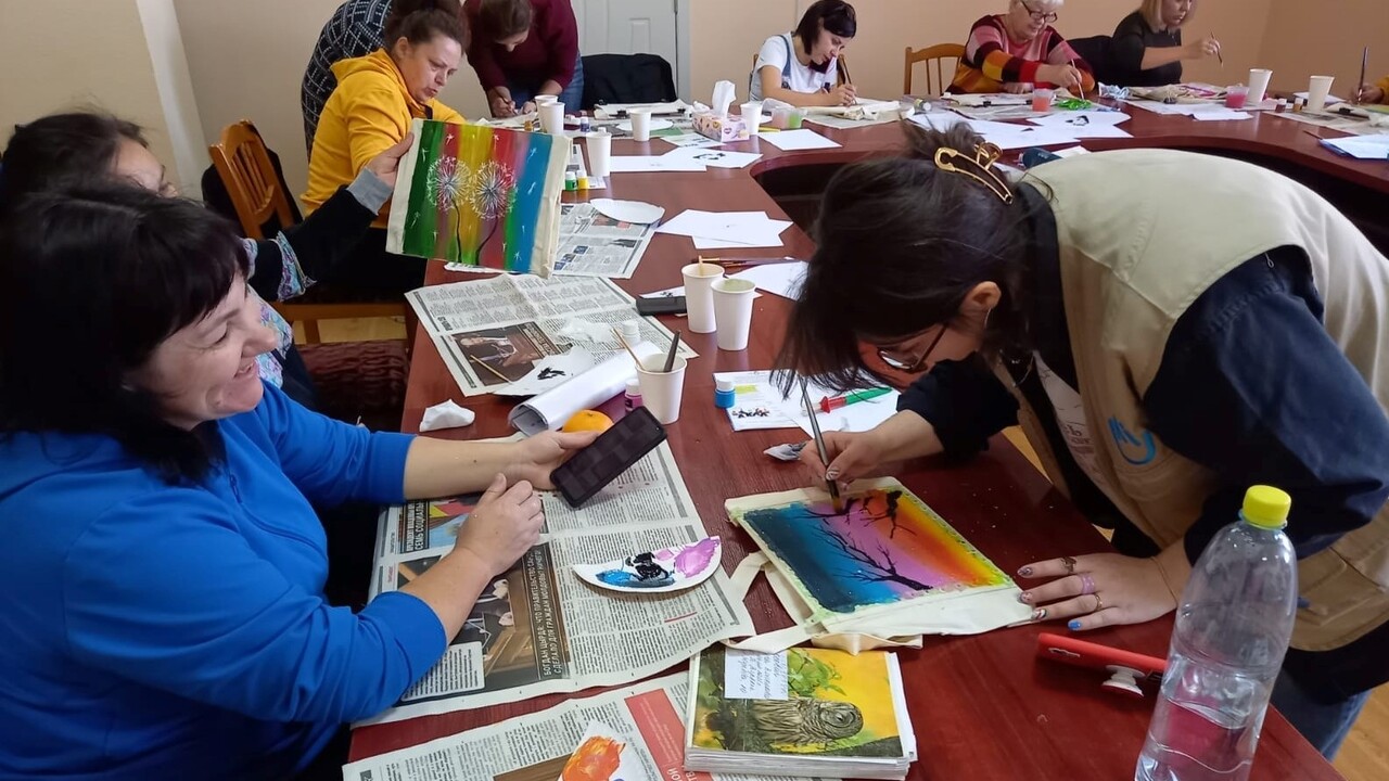  A droite, Carolina de HI et à gauche une bénéficiaire qui fait de la peinture sur des tableaux lors d'une réunion de groupe de soutien psychosocial (MHPSS). 