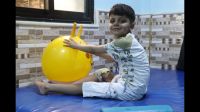 Ayham est assis sur un tapis et utilise un ballon pour l'aider dans sa rééducation.