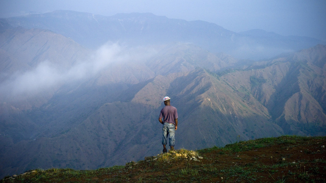 Un homme se tient de dos er regarde au loin : derrière lui, s'ouvre un paysage grandiose de montagnes dans la brume.