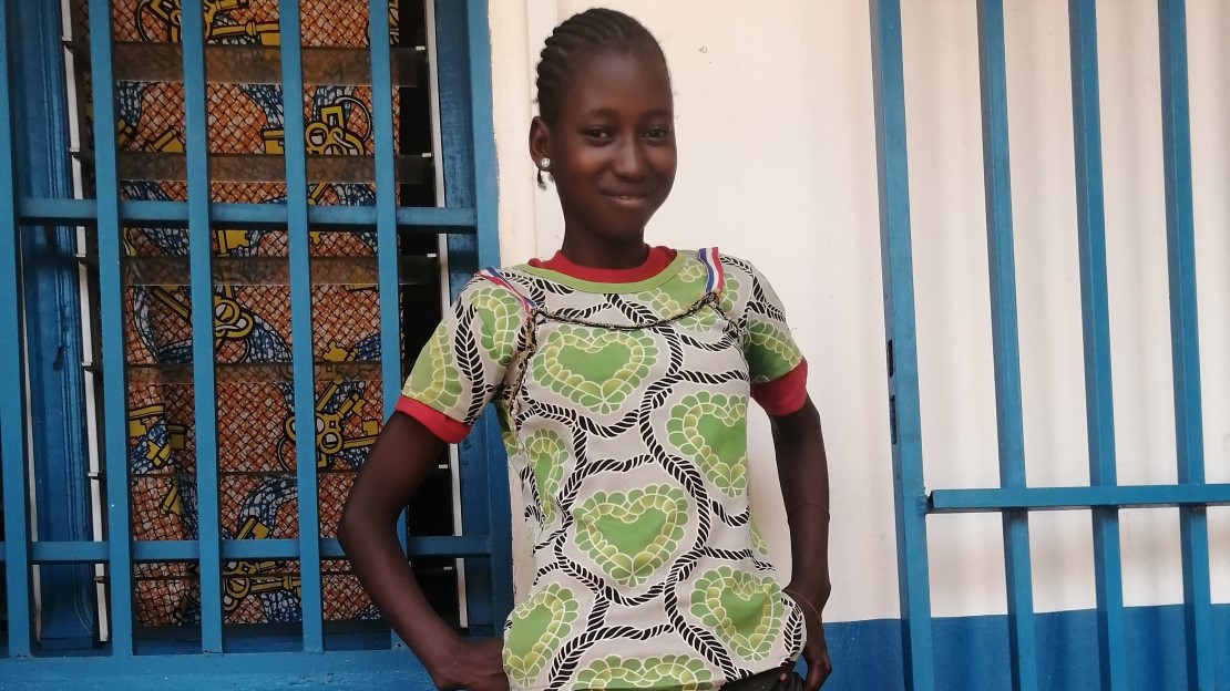 Une adolescente se tient de bout devant la salle de réadaptation de HI, elle sourit en montrant la prothèse qui lui a été fourni. 