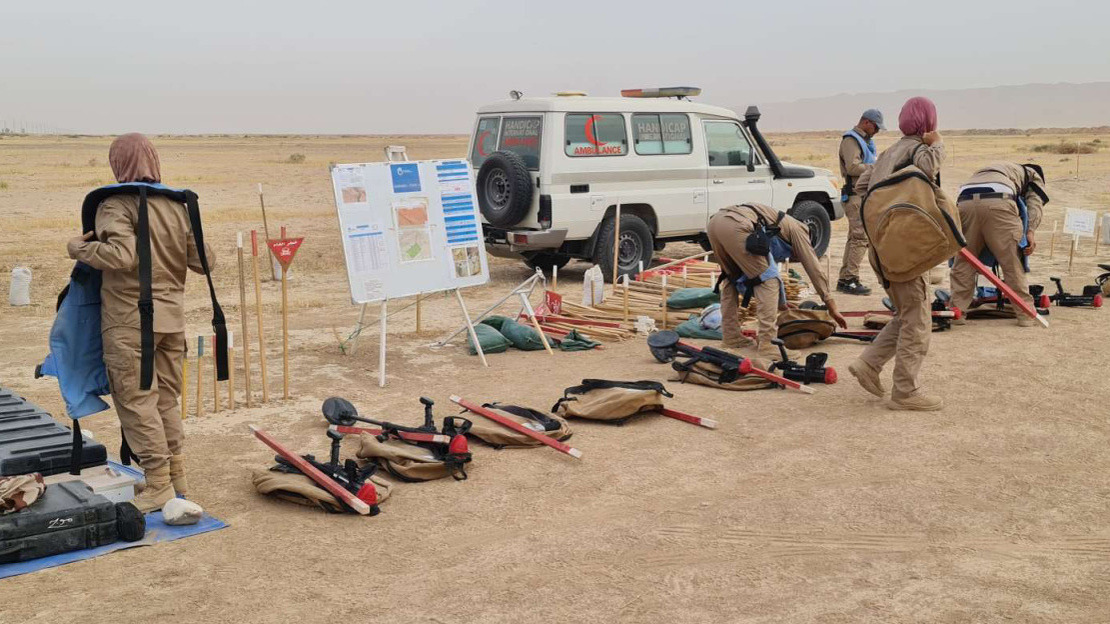 Equipe de déminage avec leur matériel , qui se préparent à partir déminer une zone. L'équipe est dans une zone qui semble déserte. 