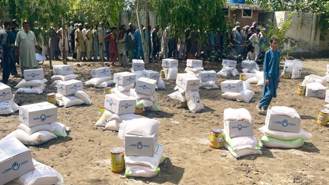 Des provisions alimentaires HI sont posées sur le sol alors que les bénéficiaires font la queue pour recevoir leurs kits.