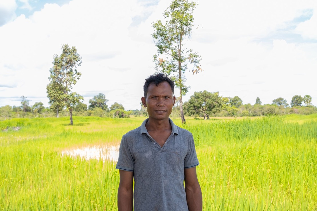Légende : Yem Yon est l'un des dix agriculteurs autorisés à remettre en culture les terres entourant le village, depuis qu'elles ont été défrichées. Yem Youn pris en photo devant une rizière  