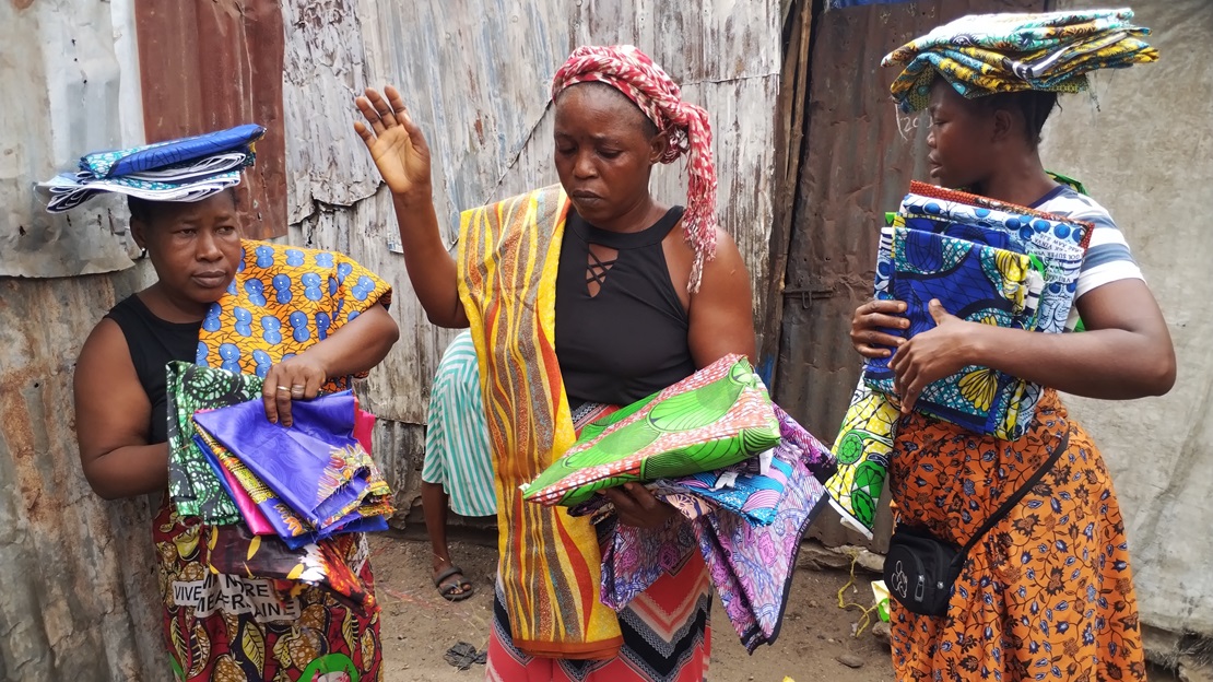 Trois femmes sont au centre de l'image, chacune porte du tissus qui servira à leur commerce.