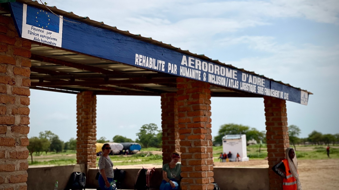 Plusieurs personnes se tiennent sous le auvent à l'entrée de l'aérodrome réhabilité.