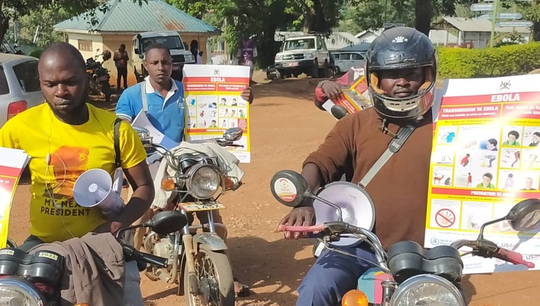 Des hommes sont roulent en moto avec des affiches de prévention sur la maladie d'Ebola.