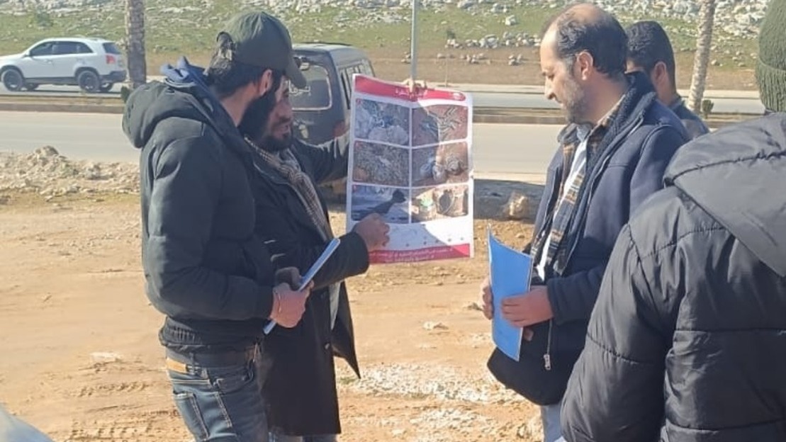 Des équipes HI montrent à deux hommes un poster avec différents exemples de munitions non explosées présentes en Syrie. 